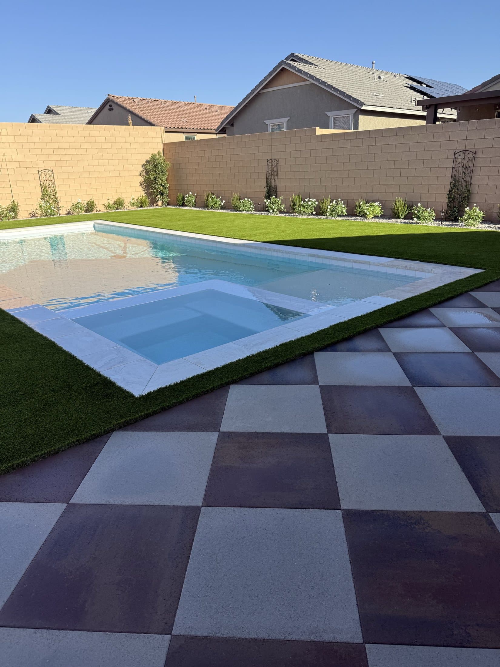 Two-tone checkerboard paver patio beside a pool and spa