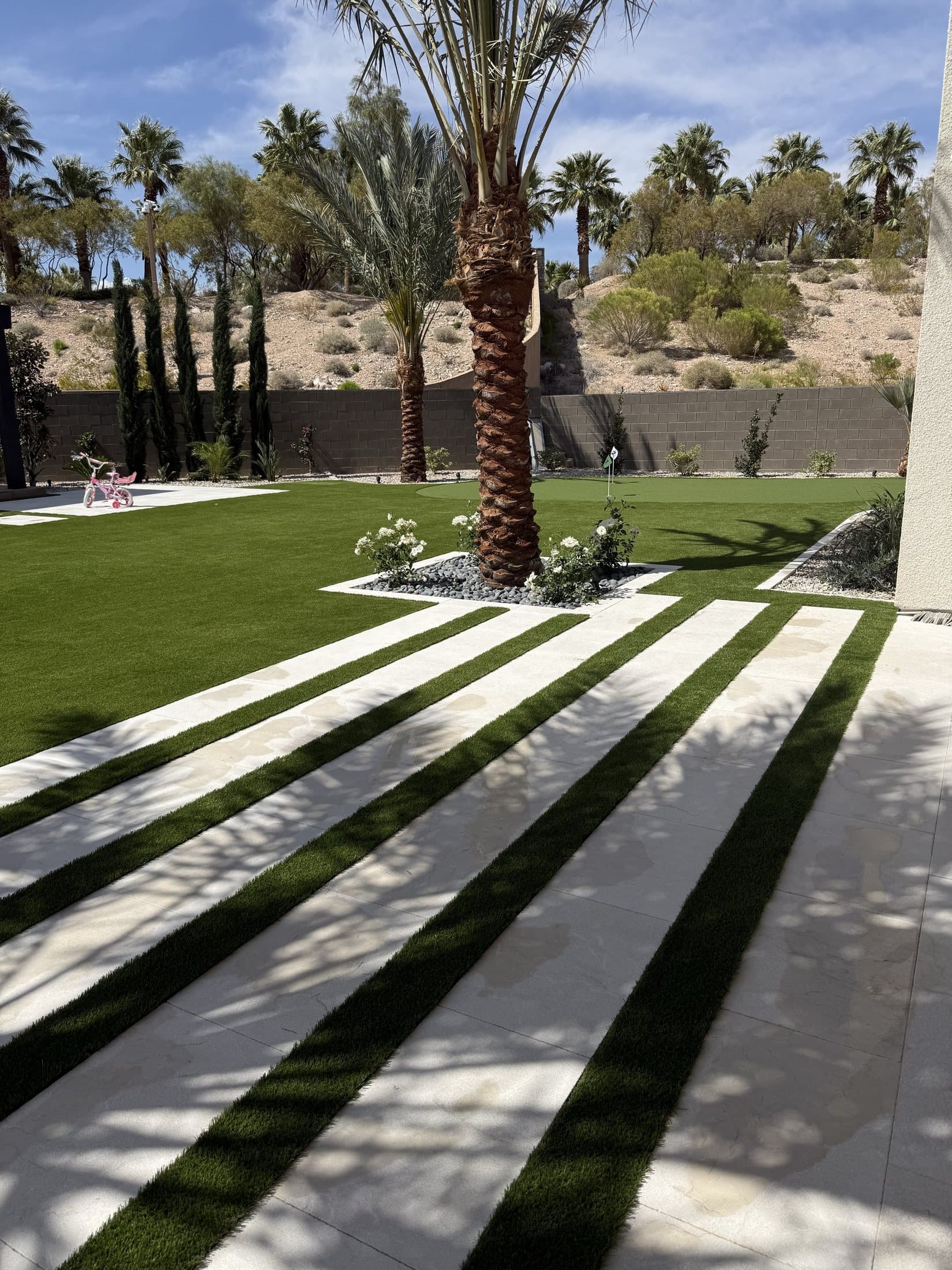 Finished backyard with striped paver-and-turf walkway, putting green, and mature palm trees