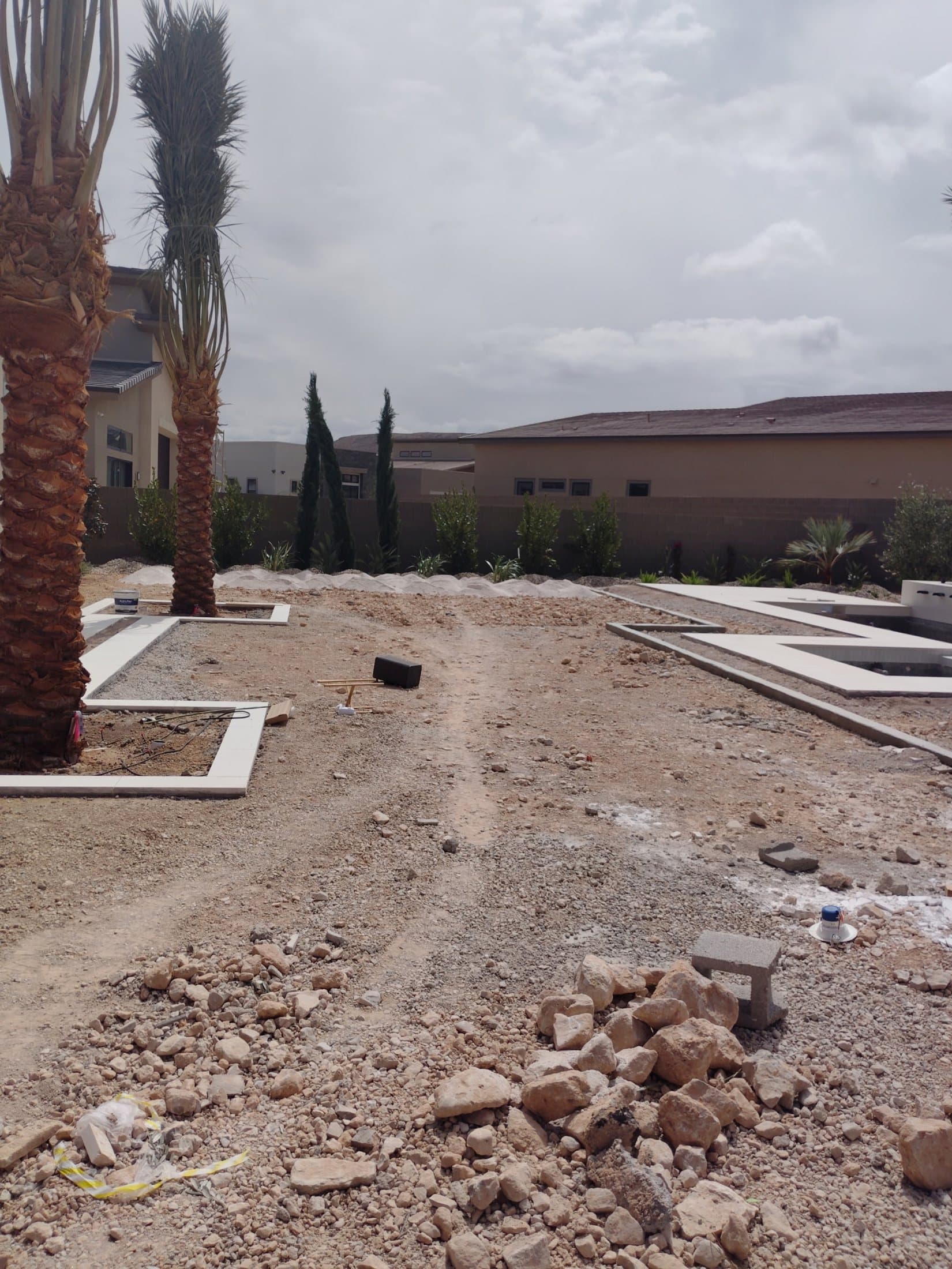 Bare dirt and gravel backyard before construction, palm trees and pool shell in place