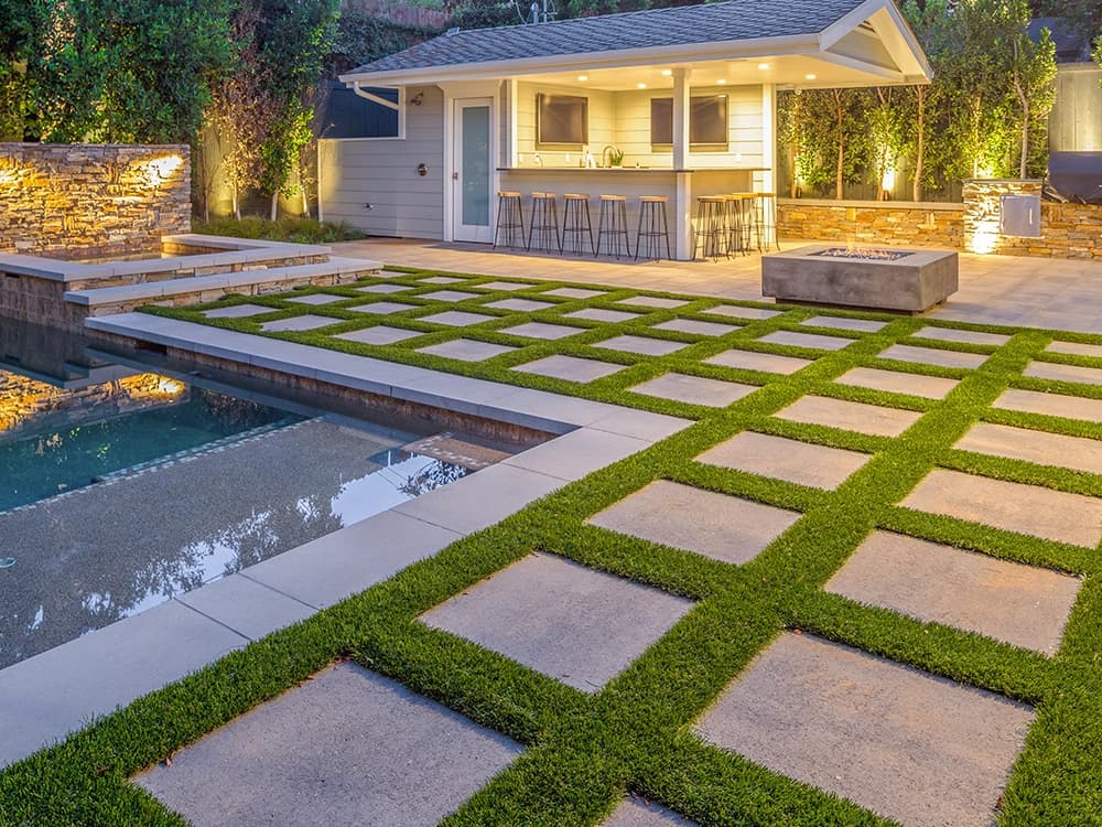 Evening paver-and-turf patio with pool house and fire pit